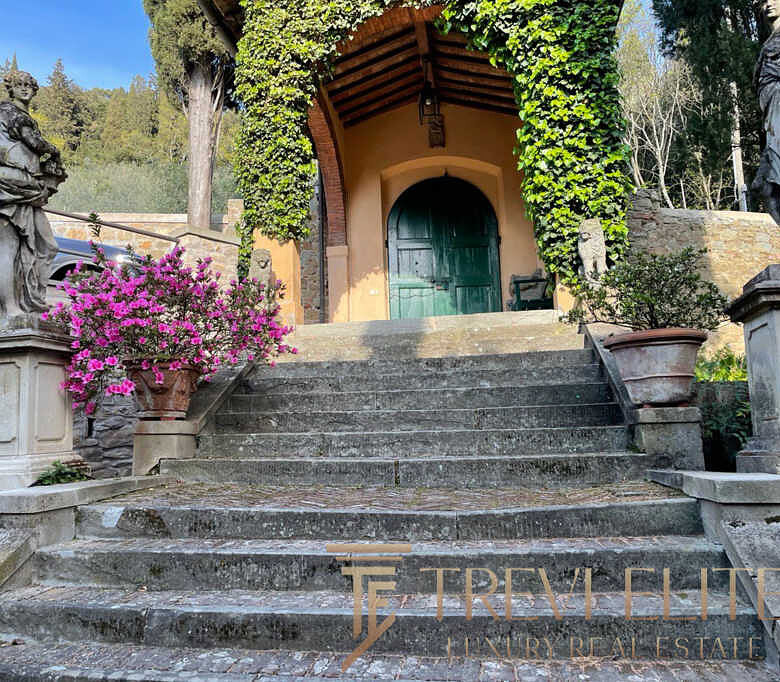 Роскошные ступеньки и статуи у входа в исторический особняк с зелёной дверью, окружённые цветущими растениями на территории элитной недвижимости в Италии.