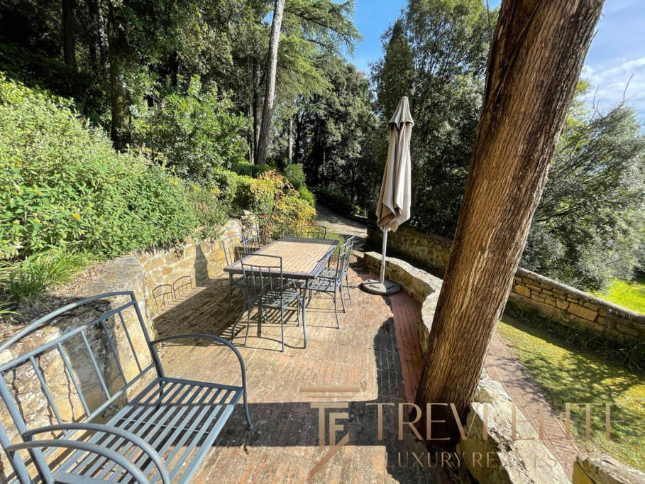 Уютная терраса на природе с деревянным столом, металлическими стульями и зонтом, окруженная зеленью и деревьями, идеально подходит для отдыха и приятных встреч на свежем воздухе.