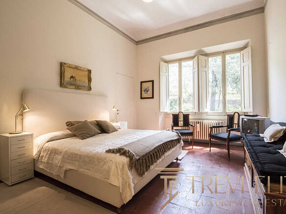 Уютная спальня с мягким светом и классической мебелью, большие окна пропускают много естественного света, создавая теплую атмосферу, идеально подходящую для роскошной недвижимости.