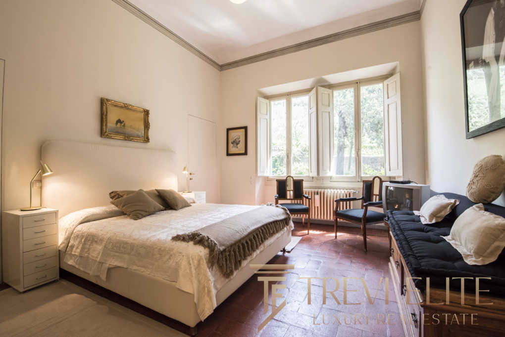 Уютная спальня с мягким светом и классической мебелью, большие окна пропускают много естественного света, создавая теплую атмосферу, идеально подходящую для роскошной недвижимости.