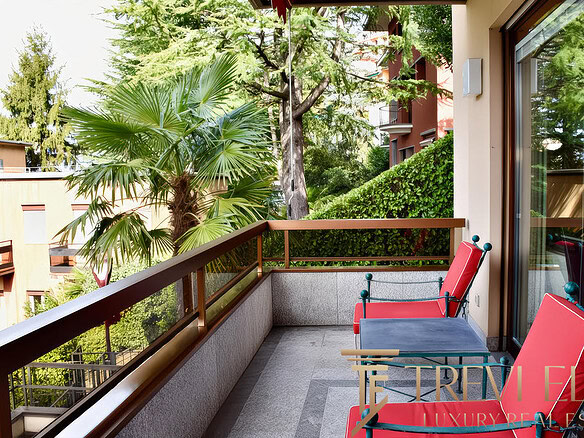 Зеленый пейзаж с деревьями и пальмами за уютным балконом современного жилого комплекса.