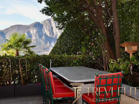 Уютная терраса с видом на горы, окруженная зеленью, идеально подходит для отдыха и наслаждения природой. В центре стоит небольшой стол и стильные кресла, создающие атмосферу уюта на открытом воздухе.