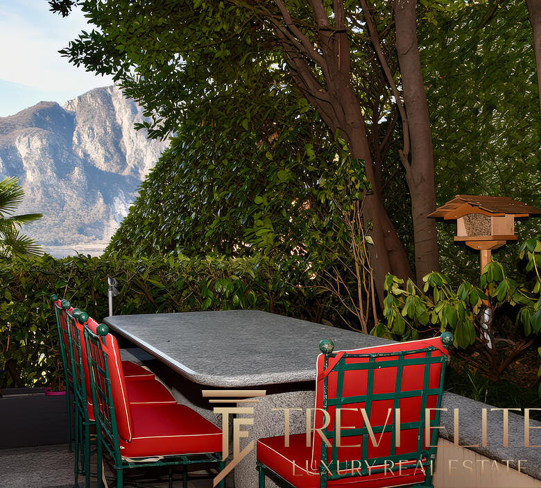 Уютная терраса с видом на горы, окруженная зеленью, идеально подходит для отдыха и наслаждения природой. В центре стоит небольшой стол и стильные кресла, создающие атмосферу уюта на открытом воздухе.