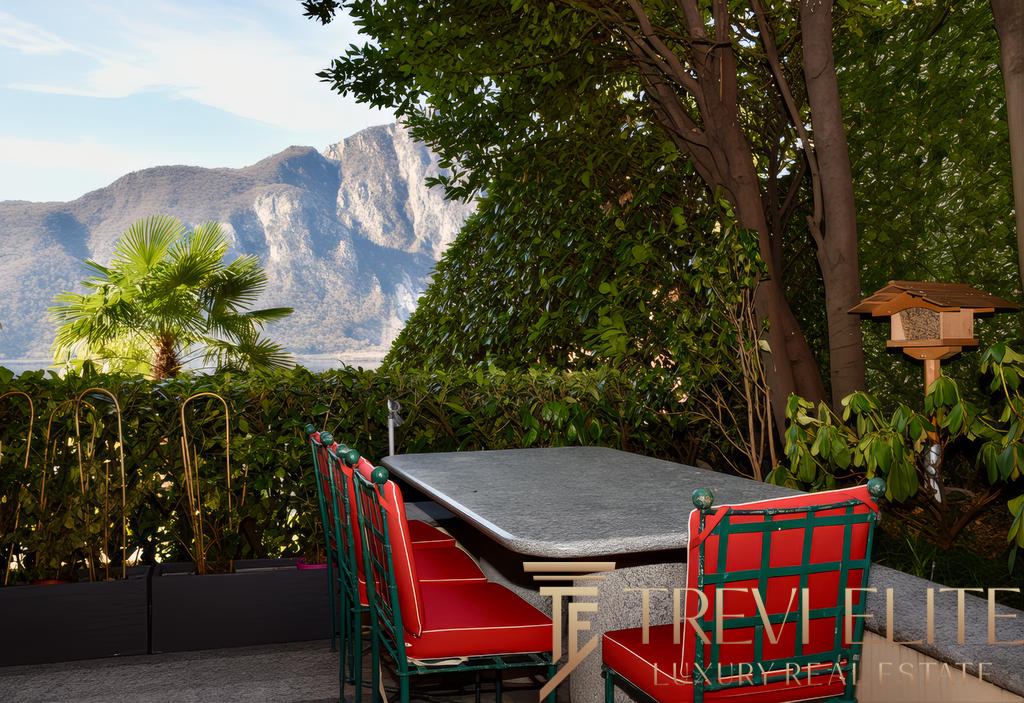 Уютная терраса с видом на горы, окруженная зеленью, идеально подходит для отдыха и наслаждения природой. В центре стоит небольшой стол и стильные кресла, создающие атмосферу уюта на открытом воздухе.