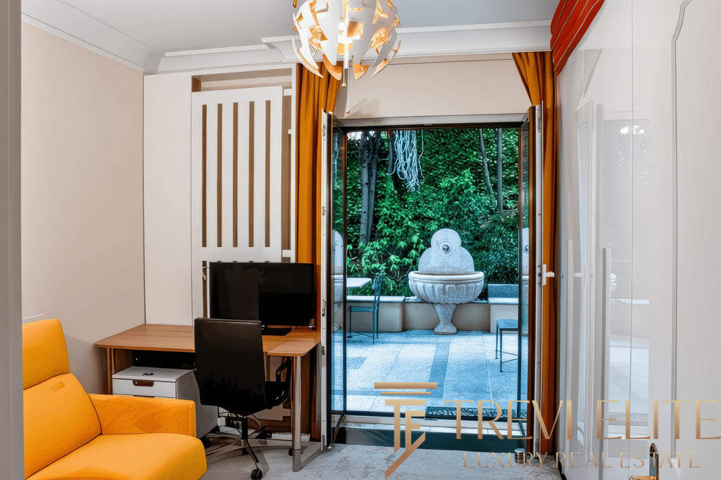 Современная квартира с выходом на террасу, интерьер с яркой мебелью и панорамными окнами, создающими уют и простор, а за стеклом — зеленый сад и декоративный фонтан.