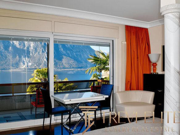 Вид из квартиры на живописное озеро и горные пейзажи через большие панорамные окна. Современный интерьер с уютной зоной отдыха и обеденной зоной, яркие акценты в декоре, создающие атмосферу комфорта и роскоши.