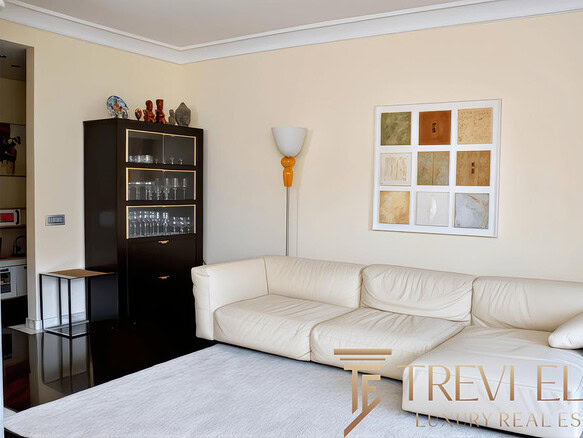 Элегантная гостиная с белым кожаным диваном, декоративным искусством и современной мебелью, создающая уютную атмосферу для отдыха.