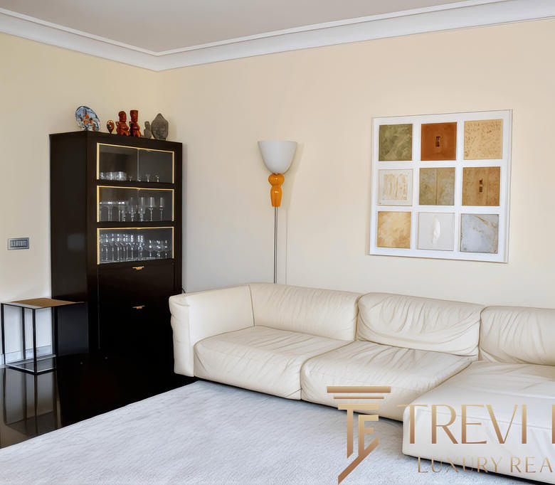 Элегантная гостиная с белым кожаным диваном, декоративным искусством и современной мебелью, создающая уютную атмосферу для отдыха.