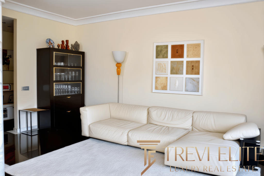 Элегантная гостиная с белым кожаным диваном, декоративным искусством и современной мебелью, создающая уютную атмосферу для отдыха.