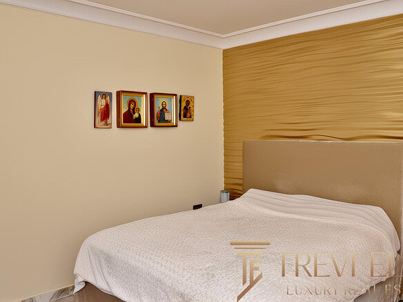 Иконы на стене в современном спальной комнате, мягкий свет, уютная обстановка, золотая текстурированная стена за кроватью, элементы религиозного декора, стильный дизайн интерьера.