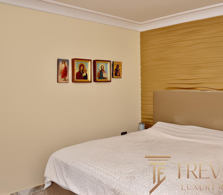 Иконы на стене в современном спальной комнате, мягкий свет, уютная обстановка, золотая текстурированная стена за кроватью, элементы религиозного декора, стильный дизайн интерьера.
