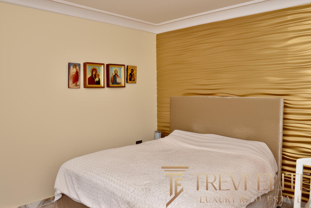 Иконы на стене в современном спальной комнате, мягкий свет, уютная обстановка, золотая текстурированная стена за кроватью, элементы религиозного декора, стильный дизайн интерьера.