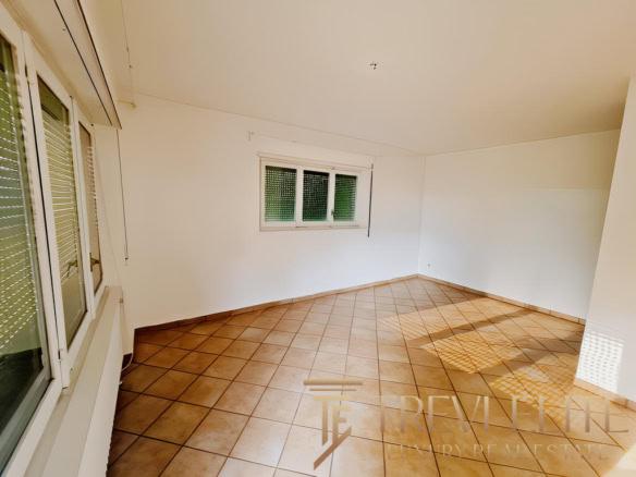 Высококачественный интерьер просторной жилой комнаты с белыми стенами и большими окнами, обеспечивающими естественное освещение, на сайте TREVI ELITE – агентство недвижимости премиум-класса.