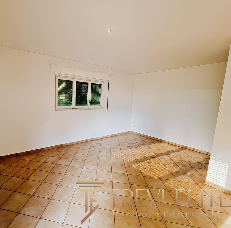 Высококачественный интерьер просторной жилой комнаты с белыми стенами и большими окнами, обеспечивающими естественное освещение, на сайте TREVI ELITE – агентство недвижимости премиум-класса.