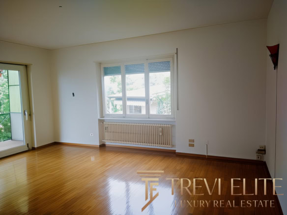 Современная уютная гостиная с большими окнами и деревянным полом, светлые стены, выход на балкон, идеально подходит для комфортной жизни.