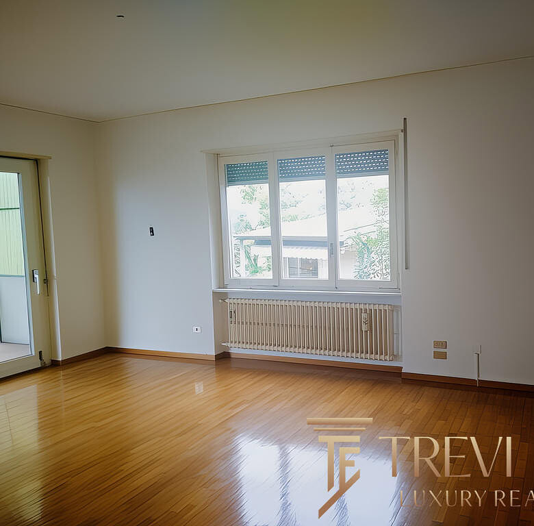 Современная уютная гостиная с большими окнами и деревянным полом, светлые стены, выход на балкон, идеально подходит для комфортной жизни.