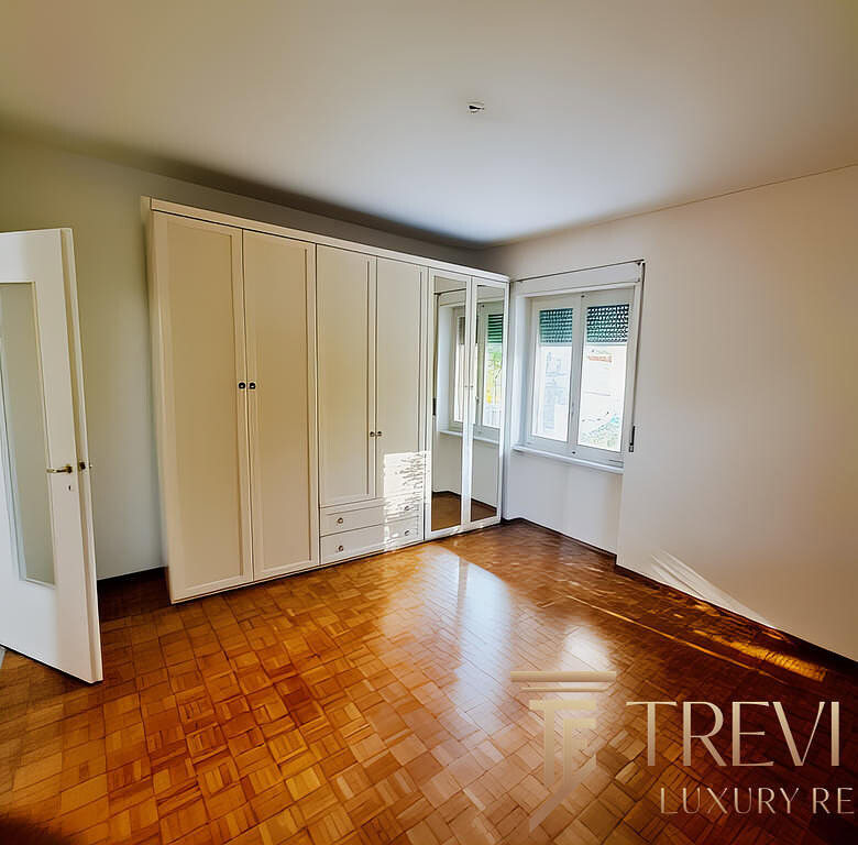 Современная уютная спальня с вместительной встроенной гардеробной и деревянным полом. Просторное окно наполняет комнату естественным светом, создавая приятную атмосферу для отдыха.