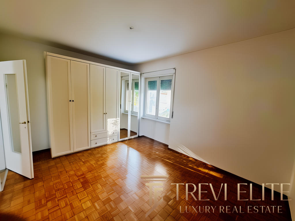 Современная уютная спальня с вместительной встроенной гардеробной и деревянным полом. Просторное окно наполняет комнату естественным светом, создавая приятную атмосферу для отдыха.