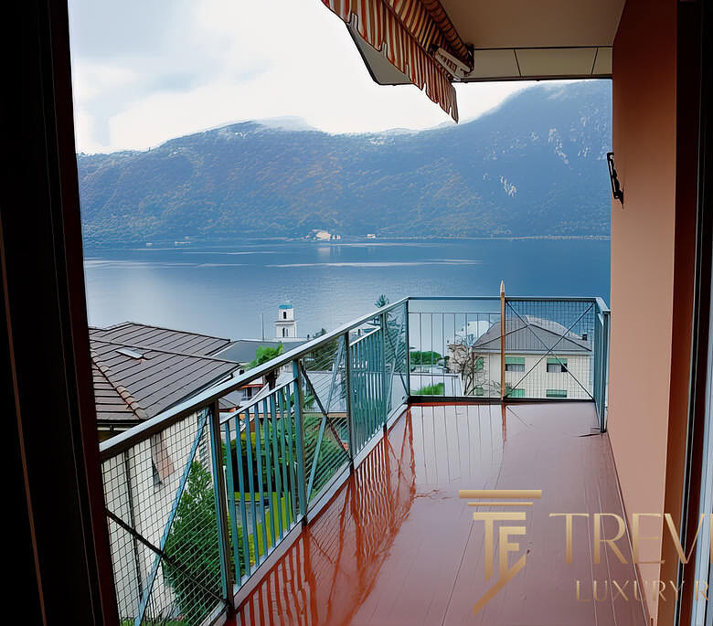 Вид с балкона на озеро и горы, уютное пространство для отдыха, современные материалы, спокойная атмосфера.
