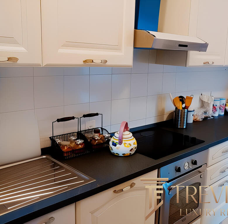 Кухонная мебель с бытовой техникой и принадлежностями в современной кухне. Желтые и голубые детали на фоне светлых шкафов. Стильный дизайн интерьера кухни.