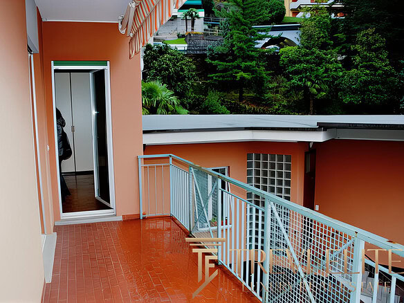 Окно балкона с видом на зелень и современные жилые комплексы, стильный интерьер, уютная уютная терраса, дощатый пол, патио, уютная зона отдыха на свежем воздухе.