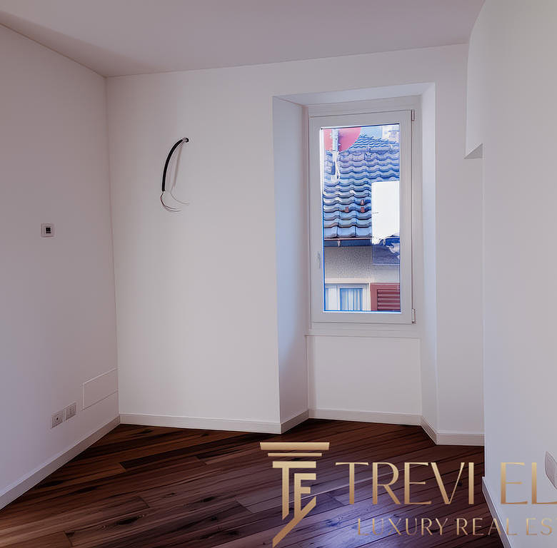 Современная пустая комната с белыми стенами и деревянным полом, окно с видом на соседние здания, идеально подходит для оформления интерьера.