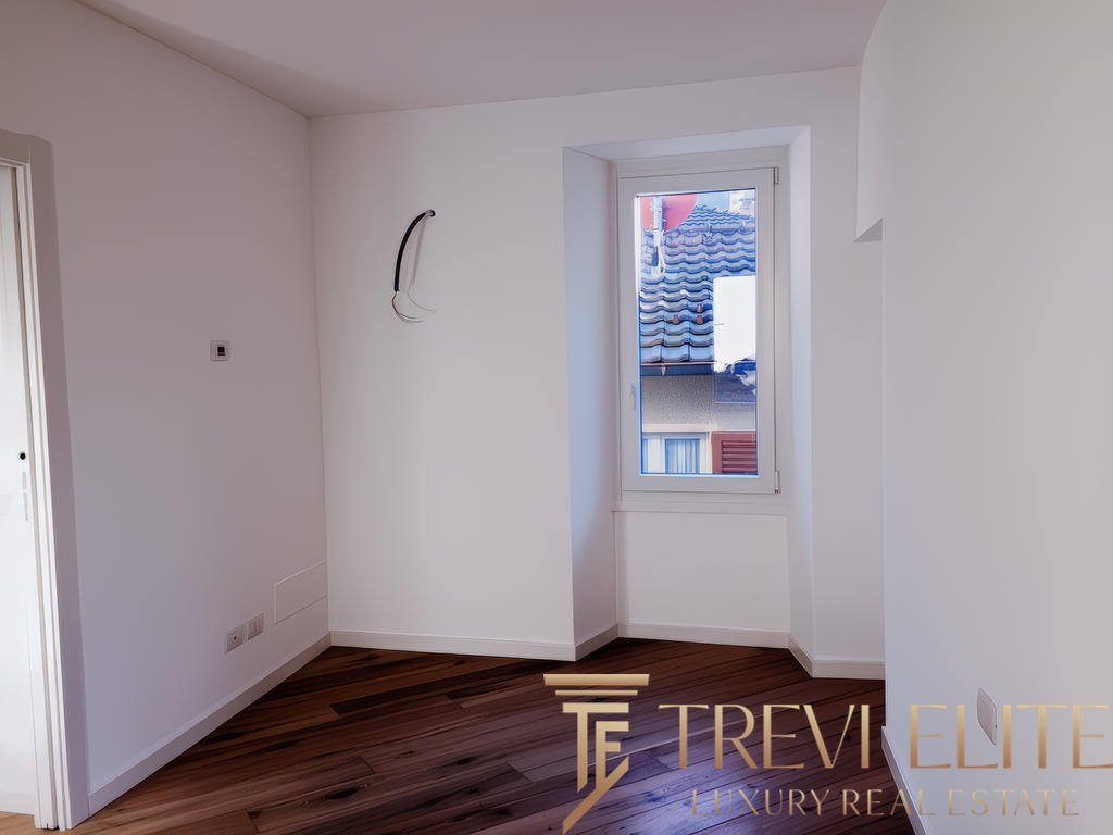 Современная пустая комната с белыми стенами и деревянным полом, окно с видом на соседние здания, идеально подходит для оформления интерьера.