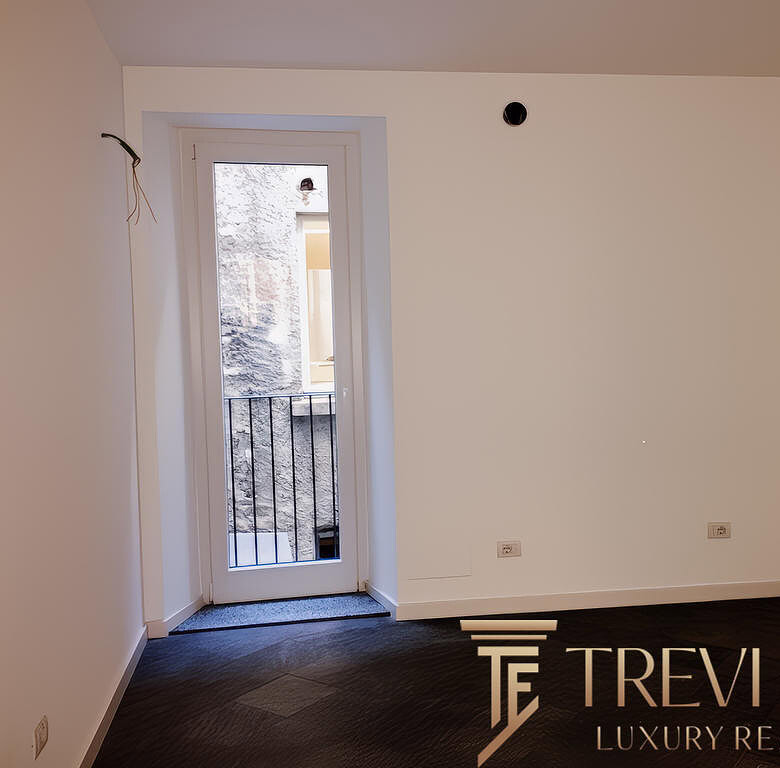 Внутренний интерьер пустой комнаты с белыми стенами, выходом на балкон и видеоконструкциями, готовыми для ремонта и модернизации, в современном жилом комплексе.