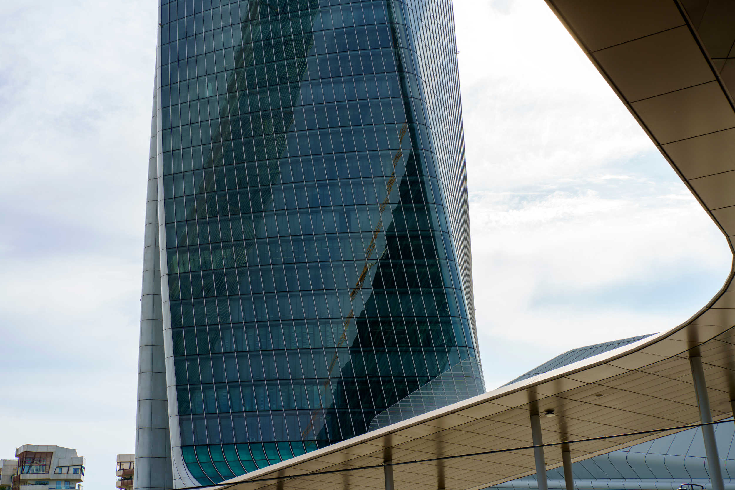 Современное стеклянное офисное здание, отражающее небоскребы и городской пейзаж, представляет архитектурную элиту и деловой центр города.