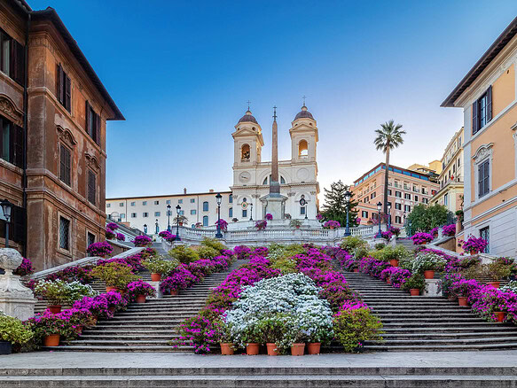 Красивые цветущие ступени с яркими петуниями и фасадами классических зданий на фоне церкви на холме в центре Рима, Италия, в солнечную погоду.