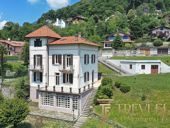 Высокий жилой дом в горной местности с террасами и балконами, окружённый зеленью и многоуровневыми участками земли, предлагает комфортное жильё в живописном районе.