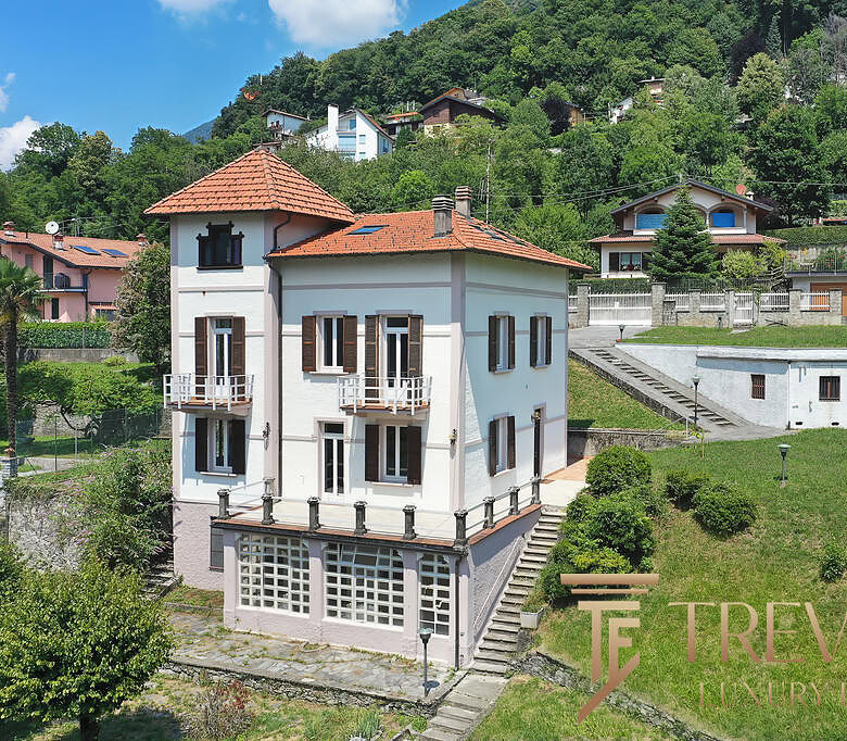 Высокий жилой дом в горной местности с террасами и балконами, окружённый зеленью и многоуровневыми участками земли, предлагает комфортное жильё в живописном районе.