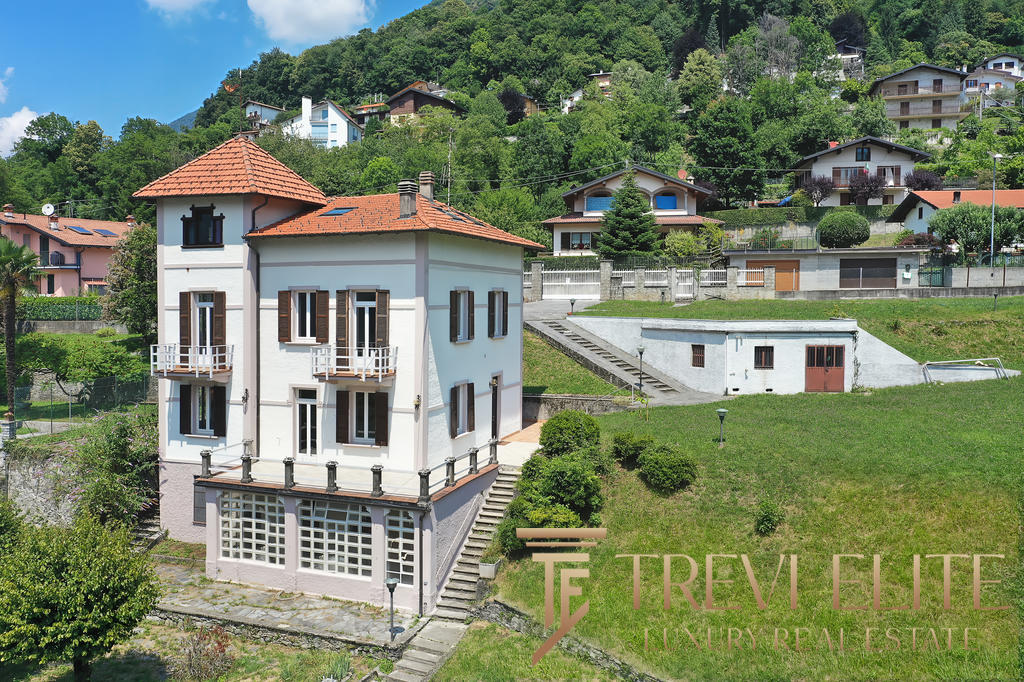 Высокий жилой дом в горной местности с террасами и балконами, окружённый зеленью и многоуровневыми участками земли, предлагает комфортное жильё в живописном районе.