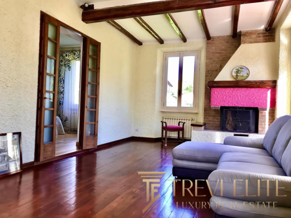 Высококачественное изображение гостиной с камином, деревянными полами и большой окном, создающее уютную атмосферу для элитного жилья.