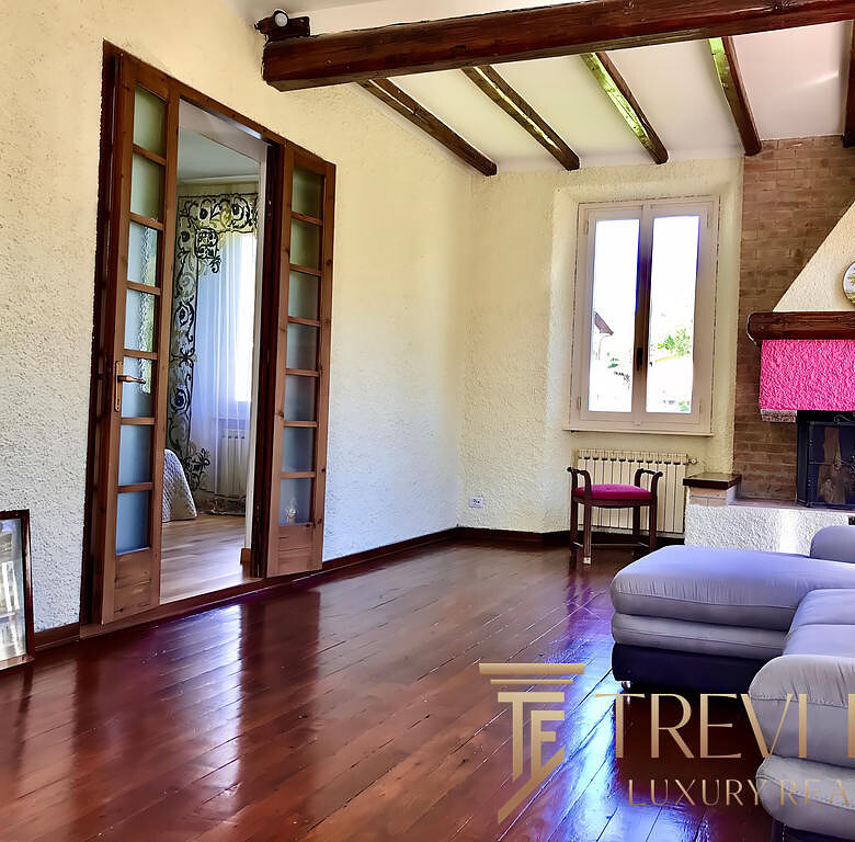 Высококачественное изображение гостиной с камином, деревянными полами и большой окном, создающее уютную атмосферу для элитного жилья.