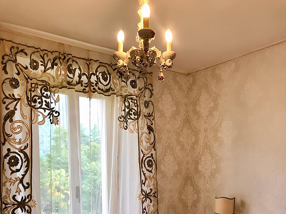 Изящная спальня с роскошными шторами, изысканным светильником и антикварным комодом, создающая атмосферу уюта и элегантности в элитной недвижимости.