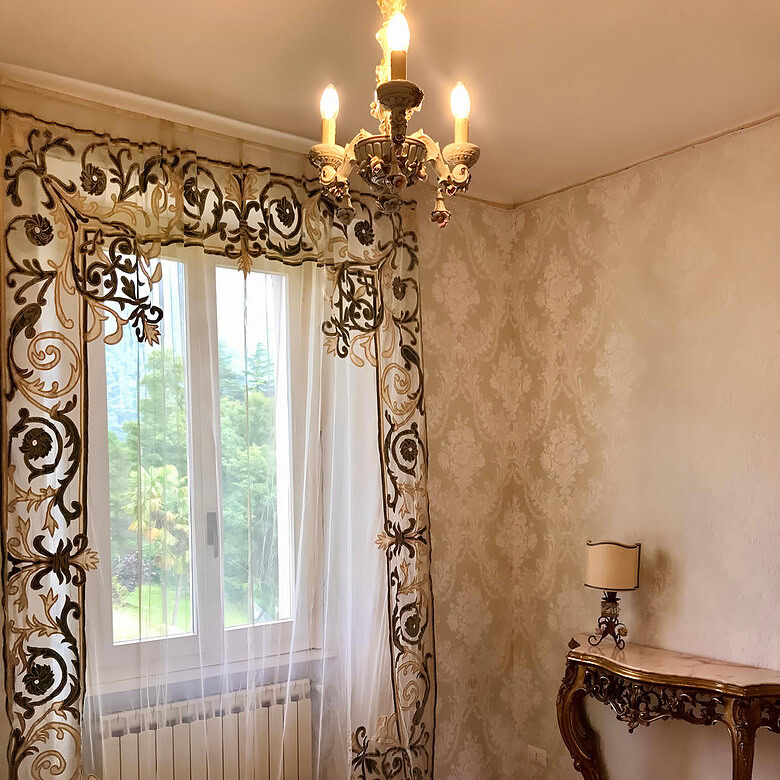 Изящная спальня с роскошными шторами, изысканным светильником и антикварным комодом, создающая атмосферу уюта и элегантности в элитной недвижимости.