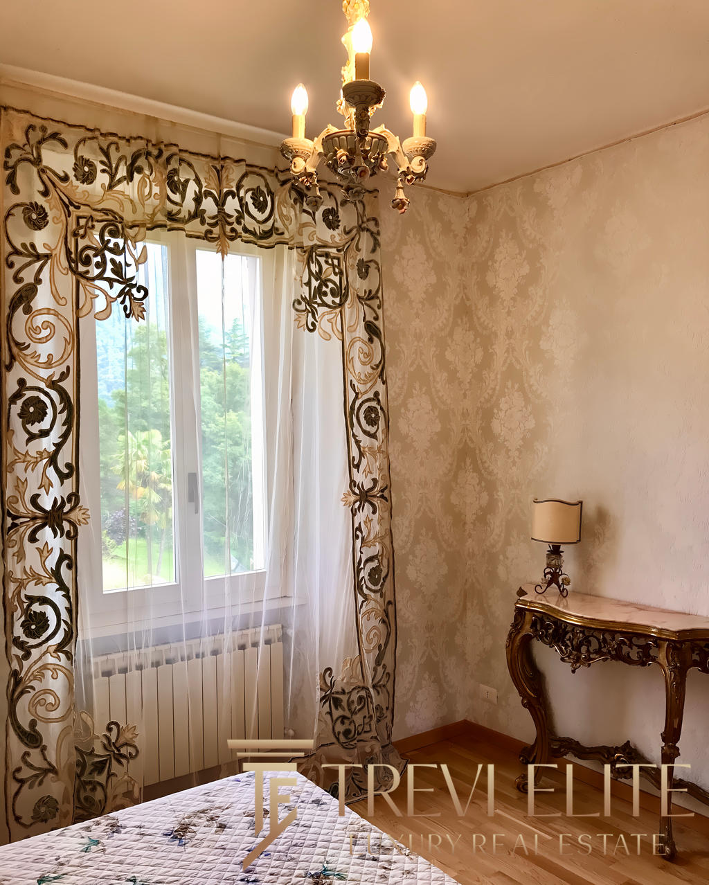 Изящная спальня с роскошными шторами, изысканным светильником и антикварным комодом, создающая атмосферу уюта и элегантности в элитной недвижимости.