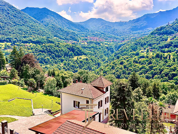 Загородный дом среди зеленых холмов на фоне гор, окруженный природой и красивыми пейзажами, идеально подходит для элитной недвижимости и комфортного проживания в живописной местности.