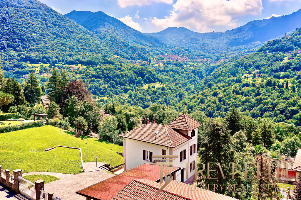 Загородный дом среди зеленых холмов на фоне гор, окруженный природой и красивыми пейзажами, идеально подходит для элитной недвижимости и комфортного проживания в живописной местности.