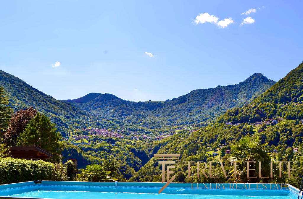 Роскошный вид на зелёные горы и живописные пейзажи с бассейном на переднем плане, идеальный для элитной недвижимости и отдыха на природе.