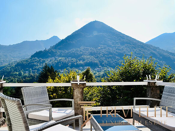 Горы на фоне, уютная терраса с креслами, панорамный вид на природу, элитная недвижимость, живописный пейзаж, роскошное жилье, Треви Элит, агентство недвижимости, элитные дома, золотая осень, отдых на природе, эксклюзивный интерьер, недвижимость в горах, панорамные окна, уютный балкон, высокое качество, комфорт и стиль.