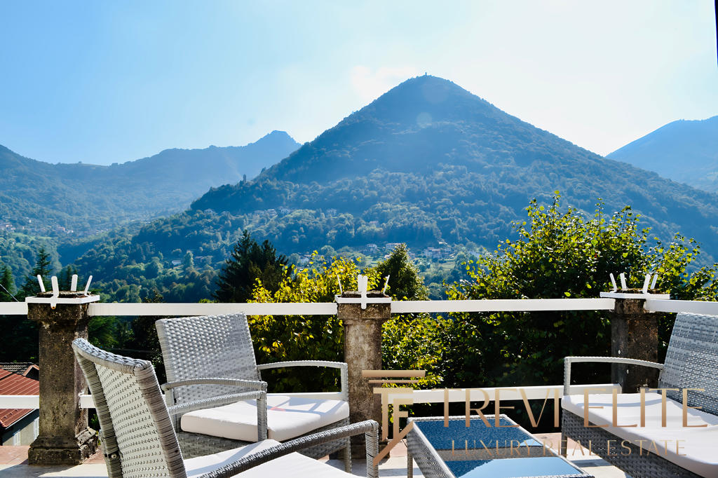 Горы на фоне, уютная терраса с креслами, панорамный вид на природу, элитная недвижимость, живописный пейзаж, роскошное жилье, Треви Элит, агентство недвижимости, элитные дома, золотая осень, отдых на природе, эксклюзивный интерьер, недвижимость в горах, панорамные окна, уютный балкон, высокое качество, комфорт и стиль.