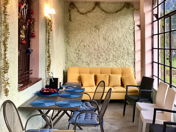 Уютная зона для отдыха и общения с декоративными елками и гирляндами, большие панорамные окна, мягкий диван и стулья, праздничное оформление интерьера в светлых тонах.