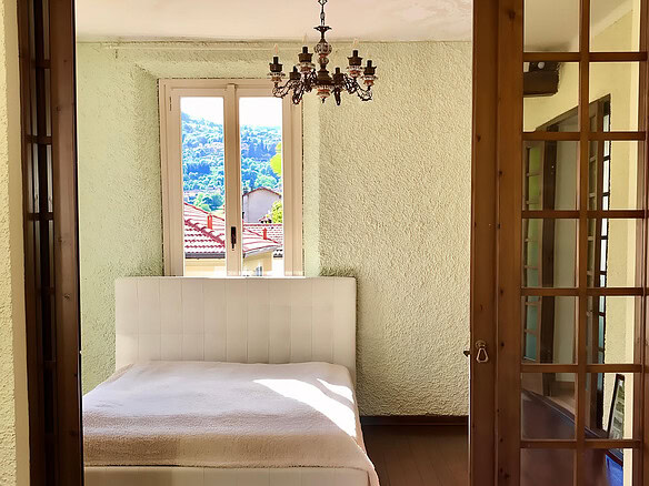 Уютная спальня с видом на природу, светлые стены и деревянный пол, просторное окно и стильная люстра, современная мебель и природное освещение, идеально подходит для комфорта и отдыха.