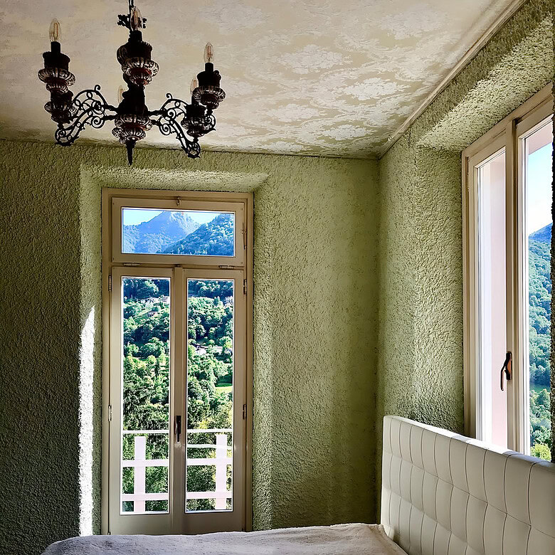 уютная спальня с панорамными окнами и видом на горы, светлые стены с текстурой, стильная люстра и мягкое постельное белье, создающее уют и комфорт в премиальной недвижимости Треви Элит.