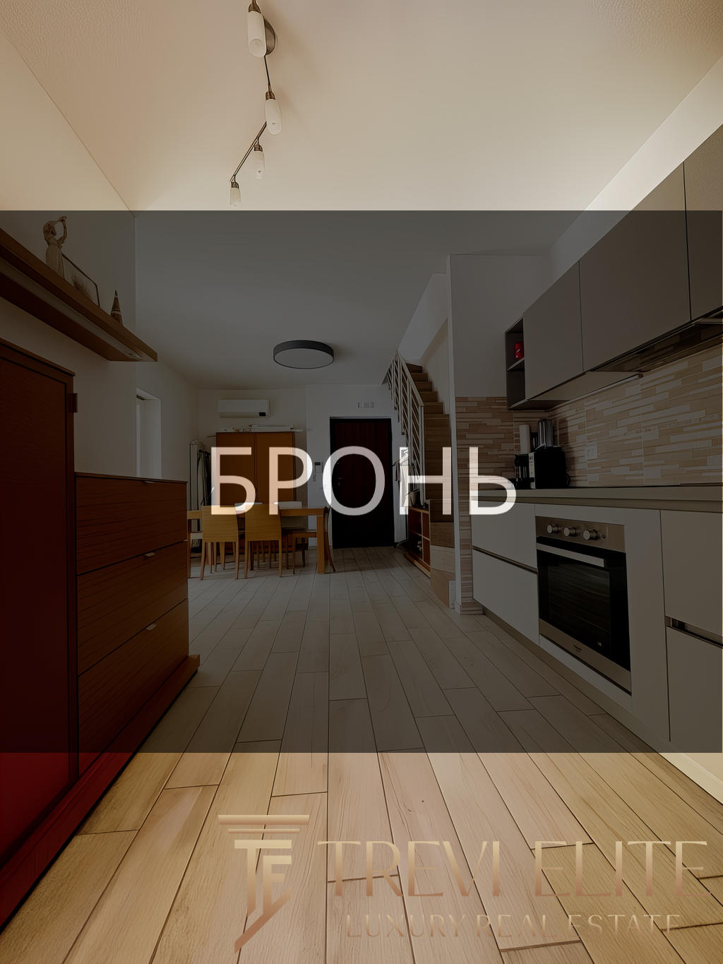 Комнатное интерьерное изображение современной кухни с деревянными полами и встроенной техникой, идеальное оформление для презентации элитной недвижимости от Треви Элит.