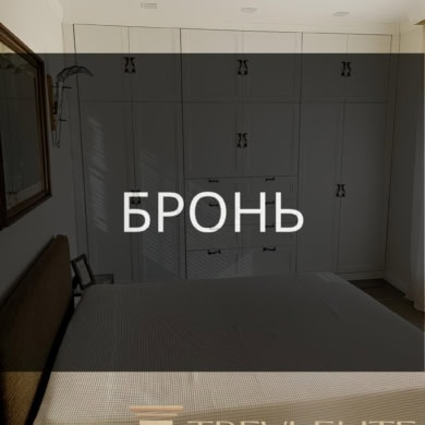 Роскошная спальня с встроенными белыми шкафами, уютной кроватью и стильными декорациями, создающими атмосферу комфорта и современного дизайна в элитной недвижимости.