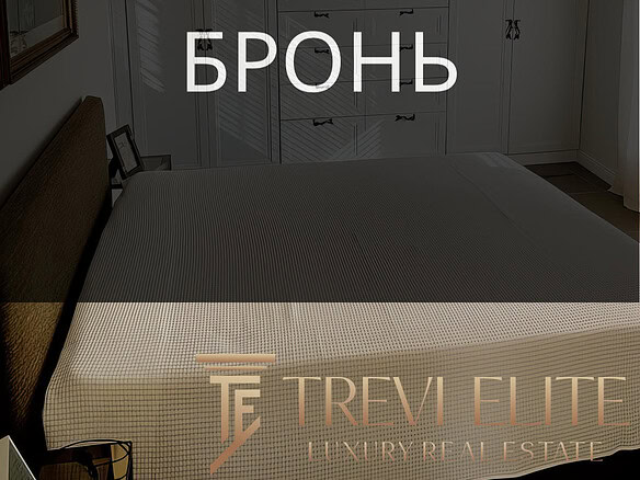 Роскошная спальня с встроенными белыми шкафами, уютной кроватью и стильными декорациями, создающими атмосферу комфорта и современного дизайна в элитной недвижимости.