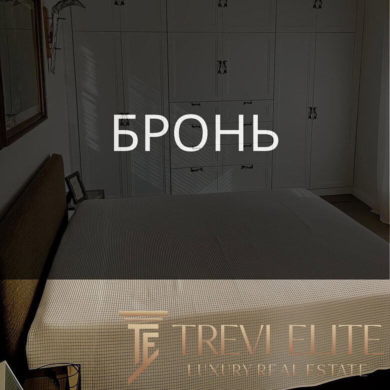 Роскошная спальня с встроенными белыми шкафами, уютной кроватью и стильными декорациями, создающими атмосферу комфорта и современного дизайна в элитной недвижимости.